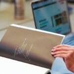 une personne tenant un livre avec un ordinateur portable en arrière-plan
