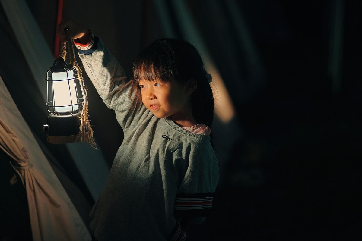 Fille asiatique dans une tente, lanterne allumée à la main, regard vers la gauche