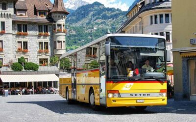 Bus jaune en mouvement sur une rue pavée dans un quartier historique avec des montagnes en arrière-plan