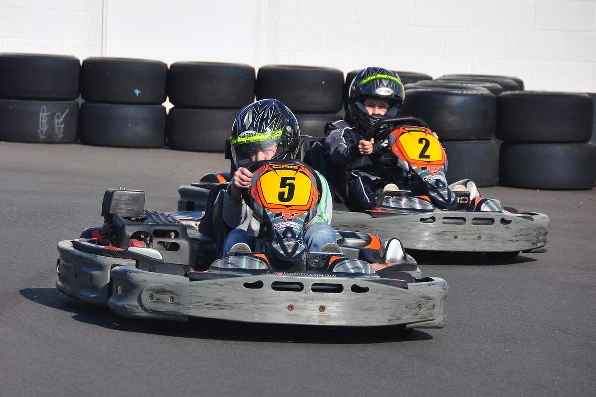 Deux enfants portent des casques et pilotent des karts numérotés sur piste