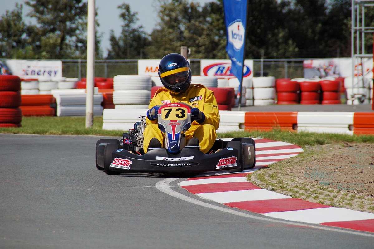 Un coureur en combinaison jaune pilote un kart sur un virage de circuit