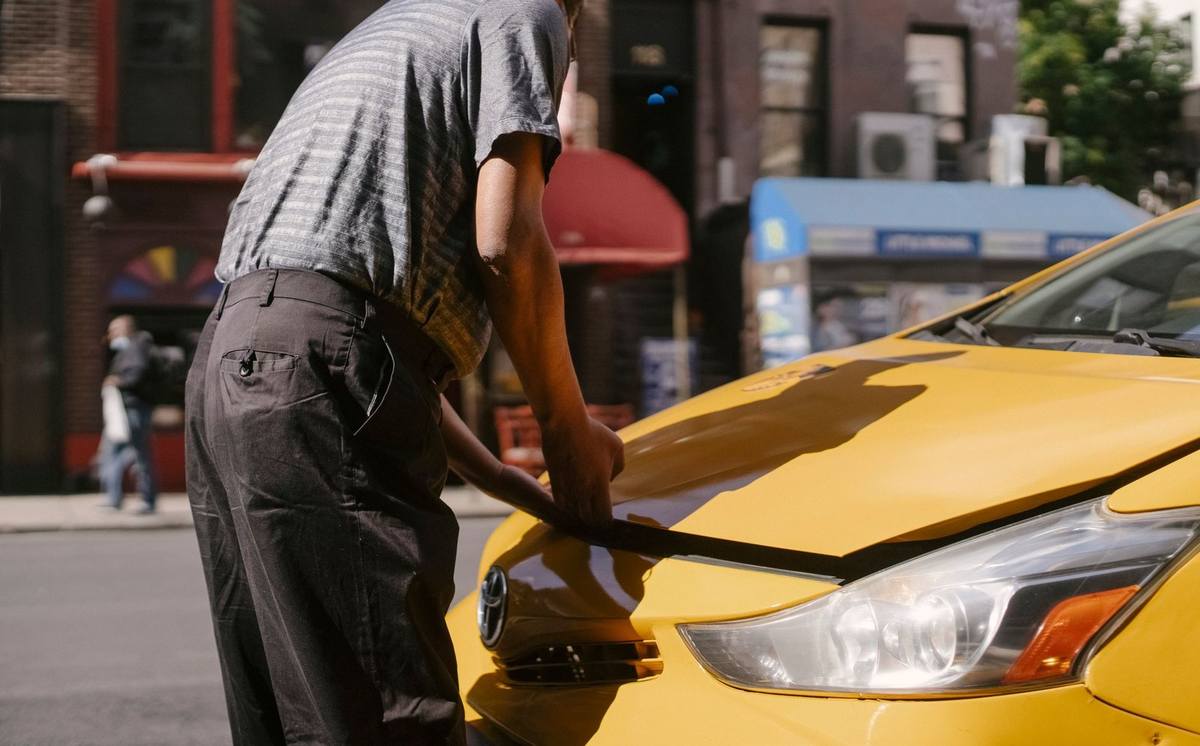 Homme ajuste le pare-chocs d'une voiture jaune sur une rue Homme ajuste le pare-chocs d'une voiture jaune sur une rue