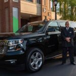 Un homme en costume noir pose devant un SUV noir