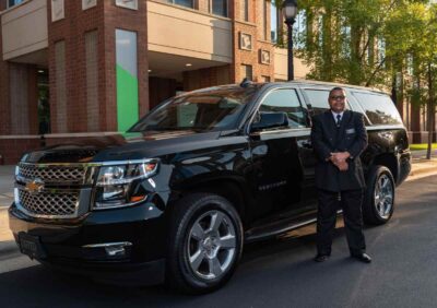 Un homme en costume noir pose devant un SUV noir