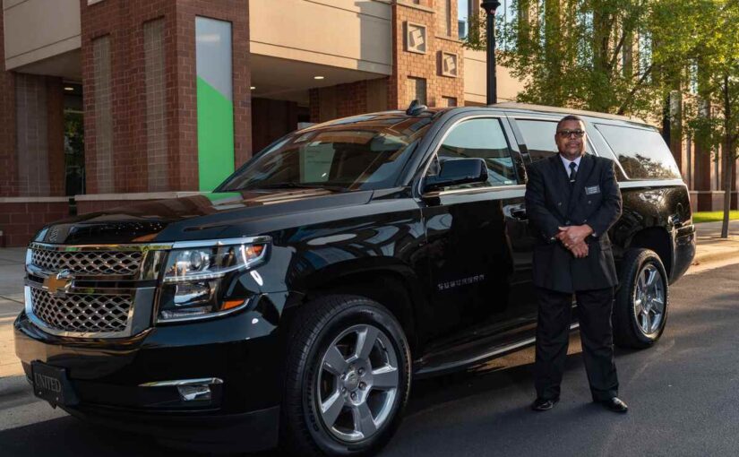 Un homme en costume noir pose devant un SUV noir